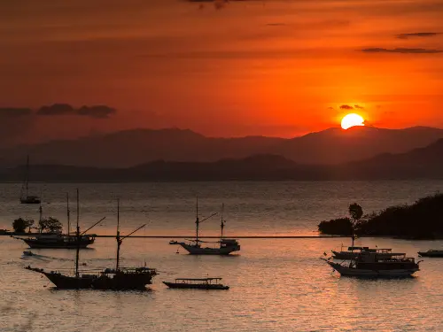 Dramatic sunset over Komodo National Park with liveaboard boats at anchor beneath colorful skies"